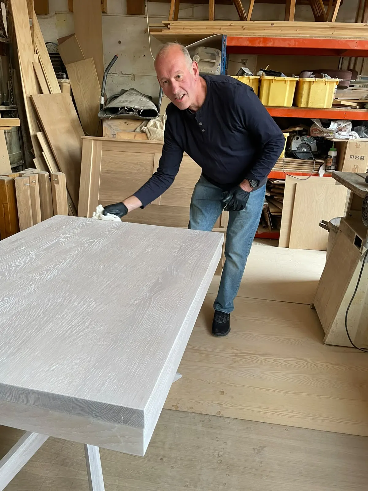 Martin Raitt wiping down the top of a pale timber table in the Greenwood workshop