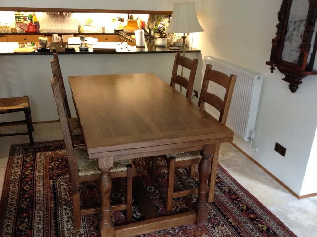 Timber dining table with turned legs and chairs on a patterned rug